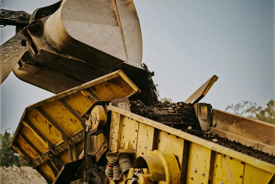 Bagger kippt Material in einen Brecher
